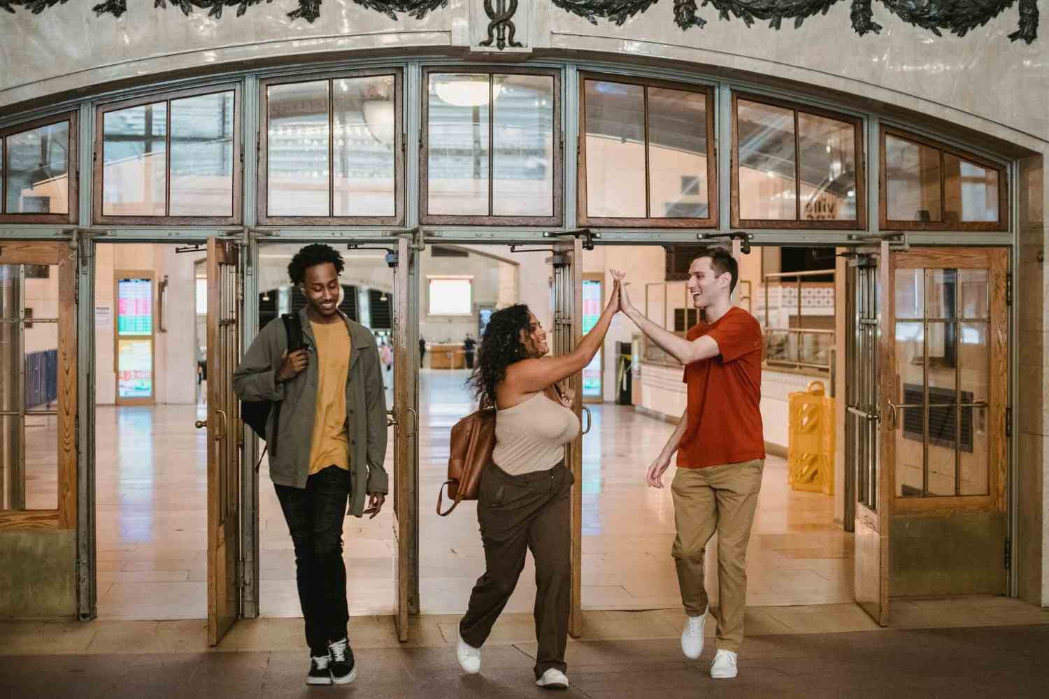 A diverse group of friends share a joyful high-five in a bustling indoor setting.